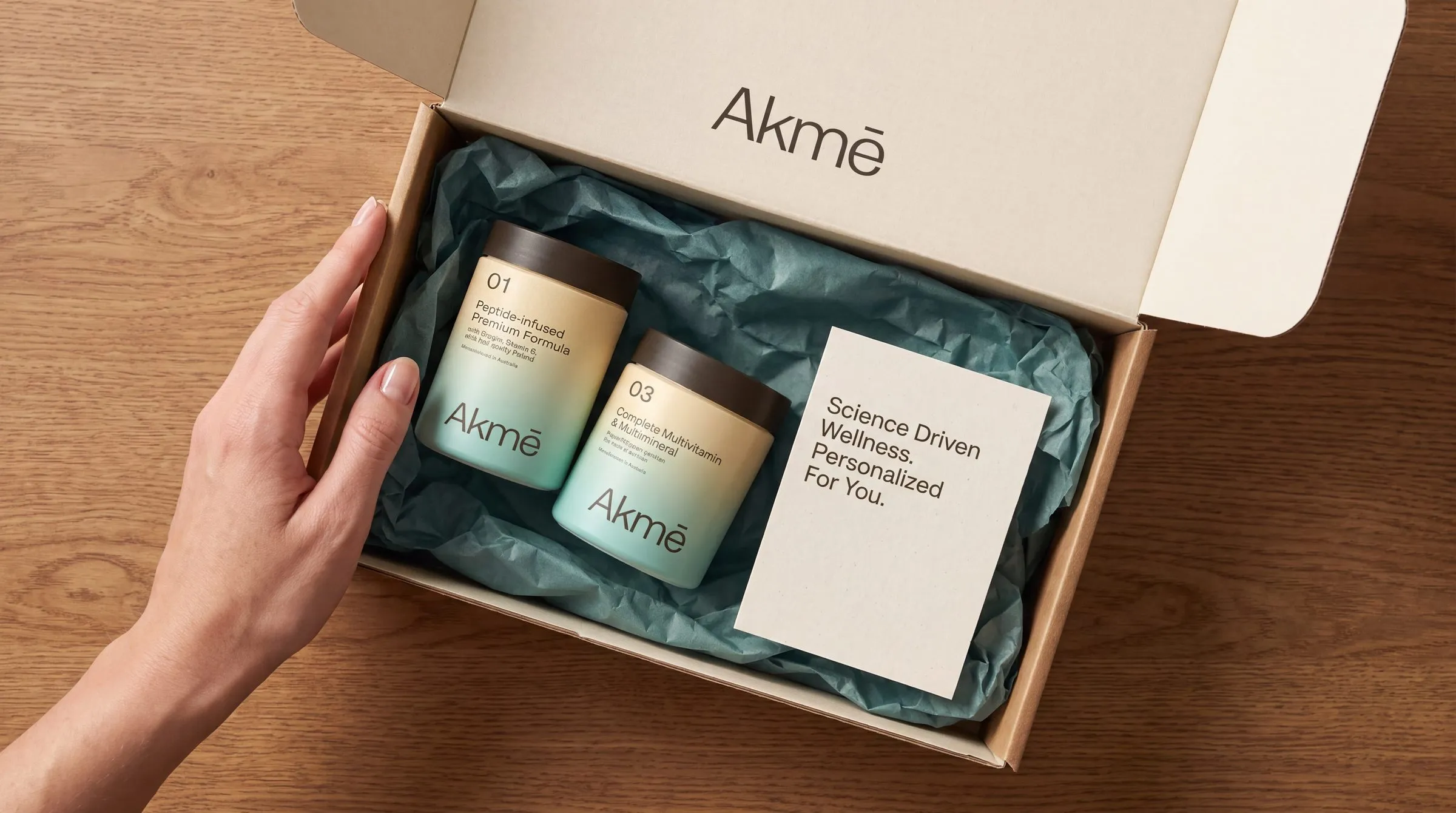 Hand opening the Akmē mailer box with jars 01 and 03 in teal tissue and a card